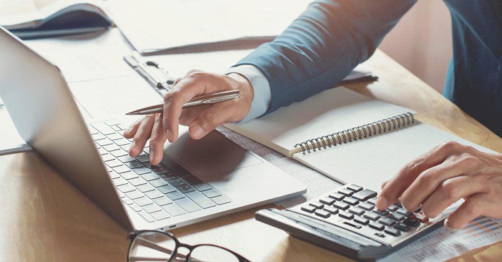 Person am Schreibtisch mit Laptop und Taschenrechner